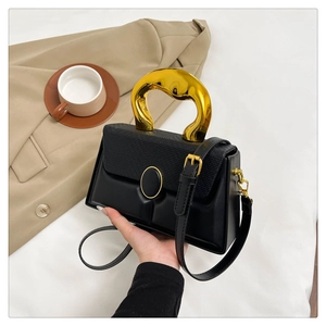 Detail of lizard-embossed black bag with a unique gold circular handle and shoulder strap