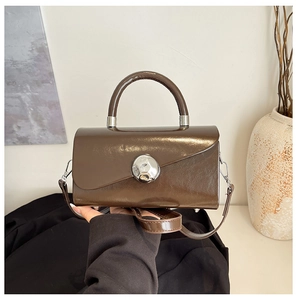 Detailed view of brown glossy leather crossbody bag with silver decorative buckle