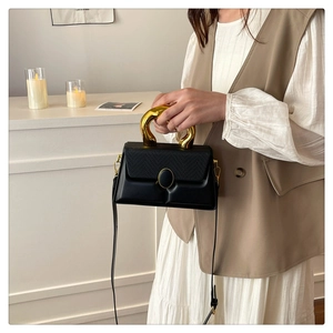 Detail of black box bag featuring woven texture flap and unique gold irregular metal handle