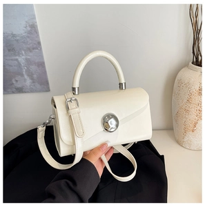 Close-up of a cream-colored structured box bag with a silver round metal clasp and top handle