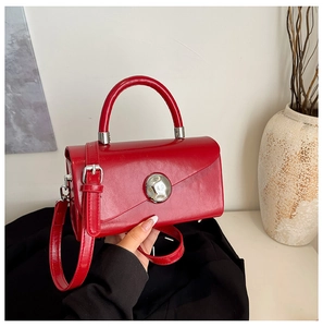 Detail of red square handbag with silver buckle and detachable shoulder strap in a minimalist setting