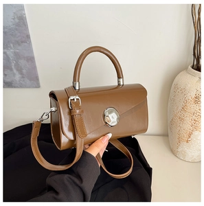 Macro detail of brown glossy crossbody bag with large silver round decorative buckle