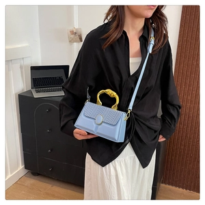 Close-up of light blue box bag featuring textured V-pattern flap and unique gold handle