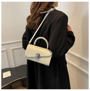 Detail view of cream structured box bag with silver circular clasp on a black blazer