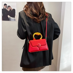 Detail of red leather crossbody bag with woven flap and golden ring metal handle