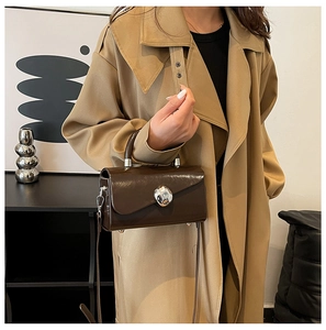 Detail of dark brown glossy square handbag with silver ball clasp on khaki trench coat