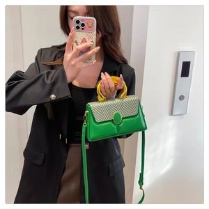 Detail of green leather handbag featuring amber-tone ring handle and woven texture lid