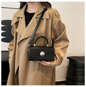 Minimalist black patent leather handbag with silver round buckle worn on khaki coat