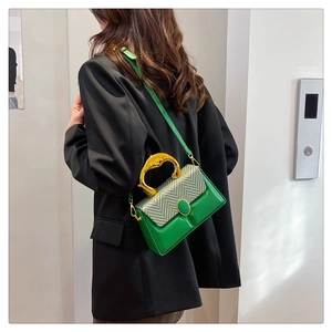 Detail of emerald green box bag featuring woven texture flap and gold wavy handle