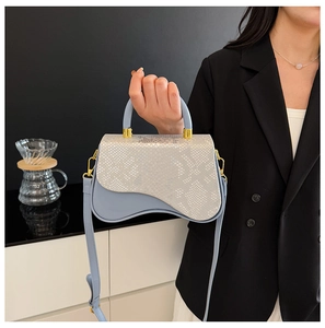 Detail of light blue crossbody bag with snake-pattern flap and gold hardware and curved base