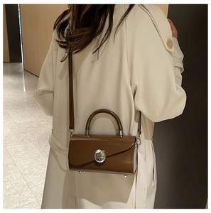 Modern dark brown square handbag with silver circular clasp on stylish beige trench coat