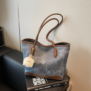 Blue denim and brown leather tote bag with gold lettering and plush monster charm