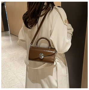 Rear view of a model carrying a glossy brown box bag with silver hardware in a hallway