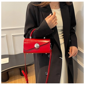 Detail of red patent leather handbag with silver metallic buckle on model in black blazer