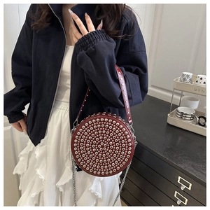 Detail view of burgundy round crossbody bag featuring silver stud rivets and a chain strap