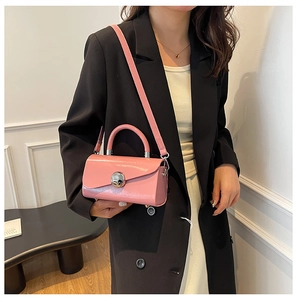 Pink glossy crossbody bag with silver sphere lock shown in a minimalist room setting
