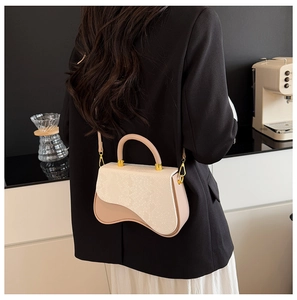 Detail showing the beige two-tone contrast box bag with asymmetric wavy bottom design