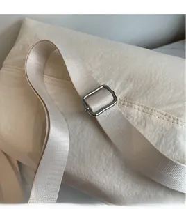 Detail of adjustable fabric shoulder strap and silver metal buckle on beige canvas bag