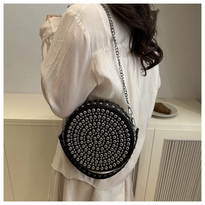 Model wearing a black round rivet crossbody bag with silver studs and metal chain strap