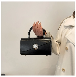 Detail of black leather box bag with large silver buckle held by model in beige trench coat