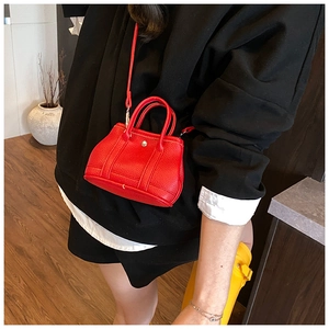 Detail view of mini red lychee pattern leather tote bag with silver buckle worn by a model