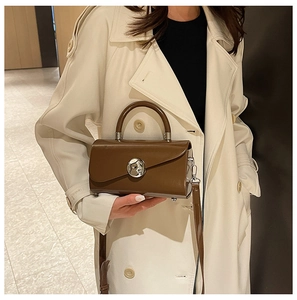 Detail of vintage brown leather box bag with silver metal disc buckle on beige coat