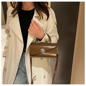 Detail of a brown patent leather crossbody bag featuring a silver circular metal lock