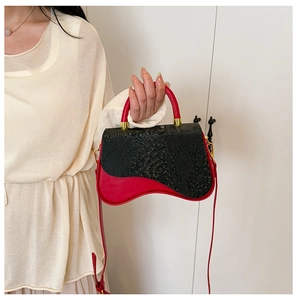 Detail of red and black color-block box bag with snakeskin texture and gold hardware