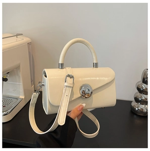 Detail of cream glossy leather box bag with a large silver spherical metal buckle handle