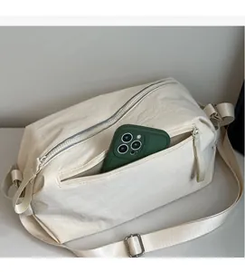 Detail of cream canvas crossbody bag showing front zipper pocket and adjustable strap