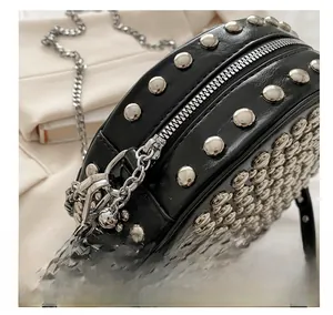 Close-up of silver metal zipper and stud details on a black round crossbody bag