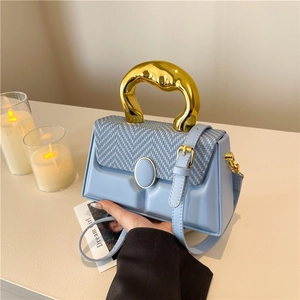 Modern light blue handbag with 3D texture and artistic golden handle on a table