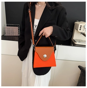 Chic orange pleated crossbody bag with brown leather flap shown in indoor lifestyle setting