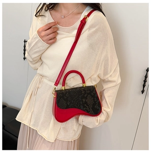 Detail of red and black snake skin pattern saddle bag with gold hardware worn by model