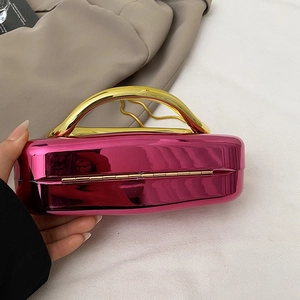 Detail of metallic rose red hard shell clutch bag with gold handle and mirror finish