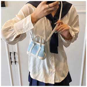 Detailed view of mini denim tote bag with white leather trim held in hand for scale