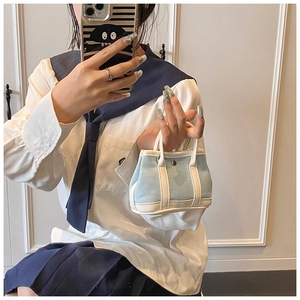 Close-up of mini blue denim handbag with white leather trim and metal button detail