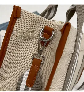 Détail du sac cabas en toile montrant les ferrures argentées et les bordures en cuir marron