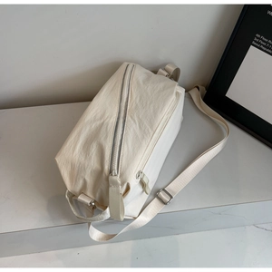 Detailed close-up of cream canvas sling bag with smooth metal zipper and adjustable strap