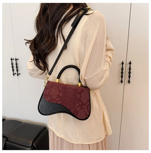 Detail of burgundy snakeskin and black leather crossbody bag worn by a model in a home