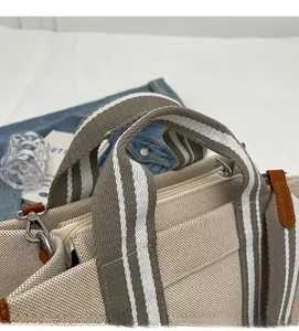 Gros plan sur la poignée en sangle rayée et le détail du zip du sac cabas en toile