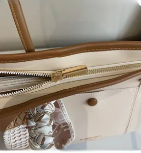 Detail of smooth gold zipper and contrasting brown trim on a beige tote bag