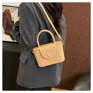 Chic beige box crossbody bag shown on a model with grey blazer and structured top handle