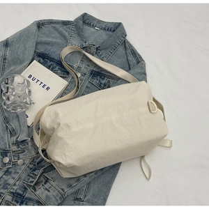 Detail of a beige nylon crossbody bag placed on a denim jacket with casual accessories