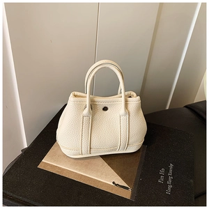 Detail of a mini cream-colored leather tote bag with classic metal snap button closure