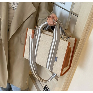 Detail of canvas tote bag with brown leather trim and striped shoulder strap in use