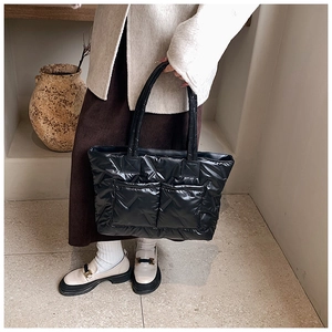 Detail of black quilted puffer tote bag featuring dual front pockets and soft padded handles