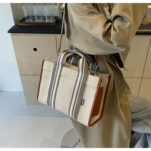 Detail of canvas tote bag showing striped woven straps and premium leather edge trim