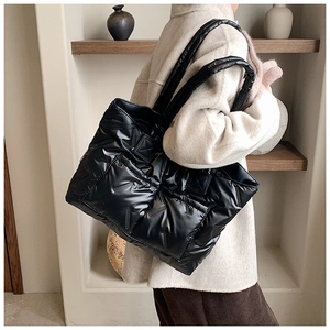 Side view of a quilted black puffer tote bag with wide straps worn by a model in a beige coat