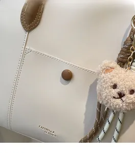 Detail of off-white tote bag with litchi texture leather and cute brown bear charm